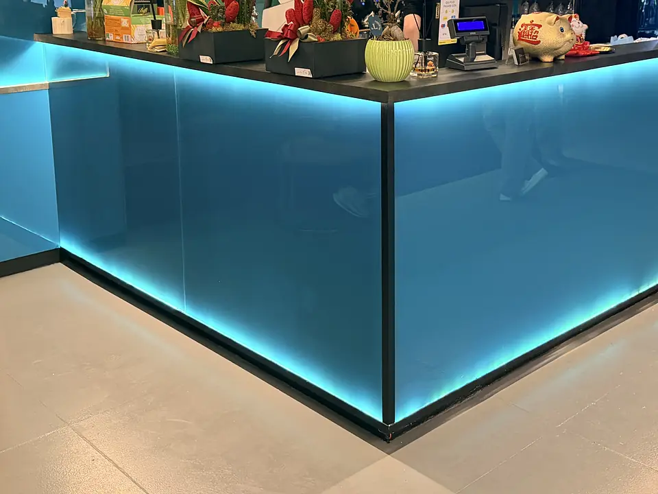 The bar counter, clad in blue glass lit from below, with plants and the till on top