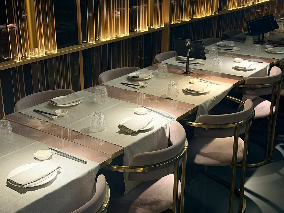 The dining room: set tables, pink chairs on gold frames and a wall of lit golden panels